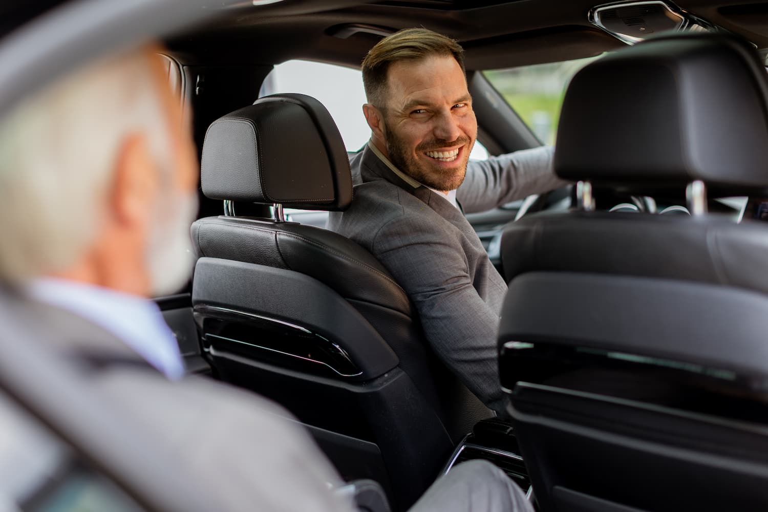 Smiling driver in a suit turning to talk with a passenger in the back seat