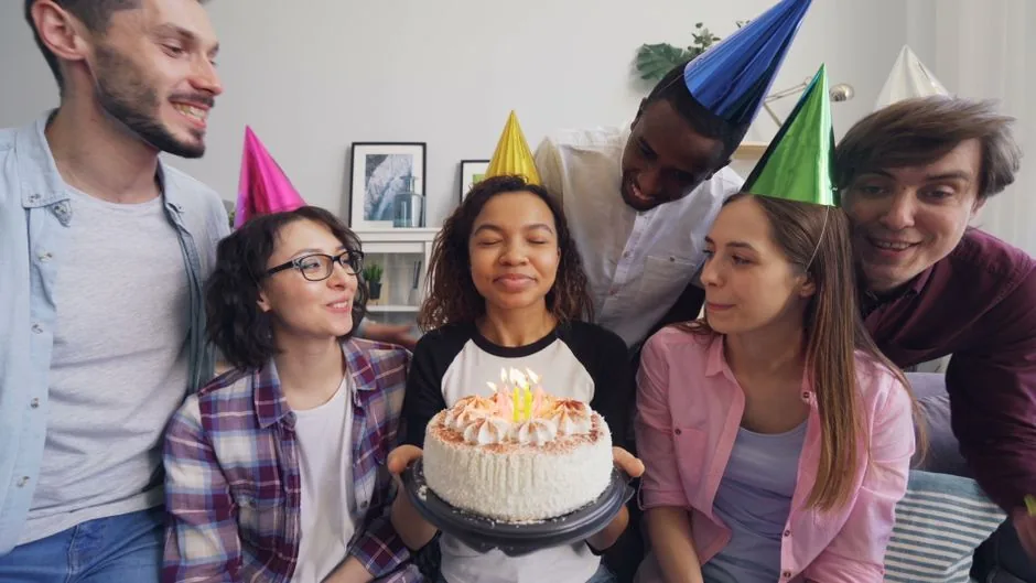 Friends in party hats around a birthday cake with lit candles