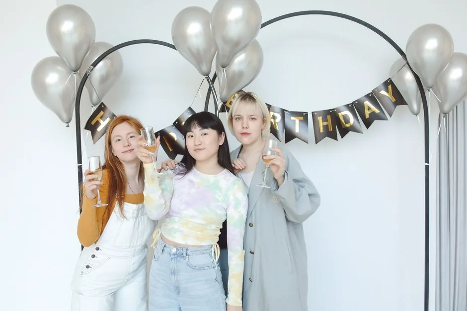 Three friends raising glasses under a birthday banner