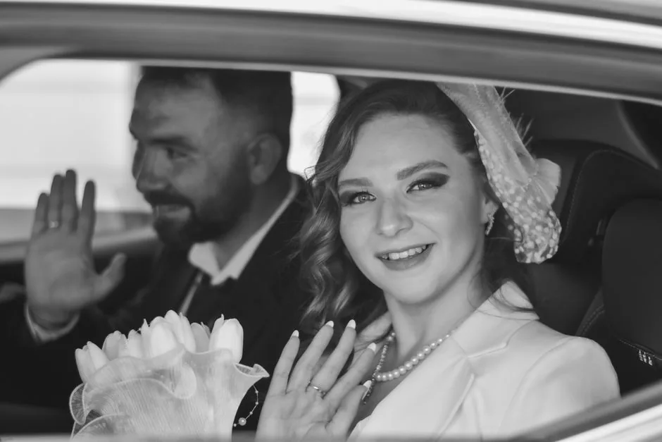 Bride and groom waving from the back seat of a car, in black and white