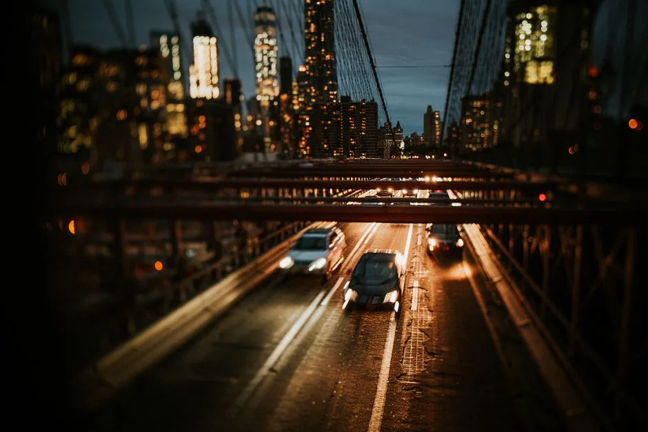 Traffic crossing the Brooklyn Bridge at night with the Manhattan skyline behind