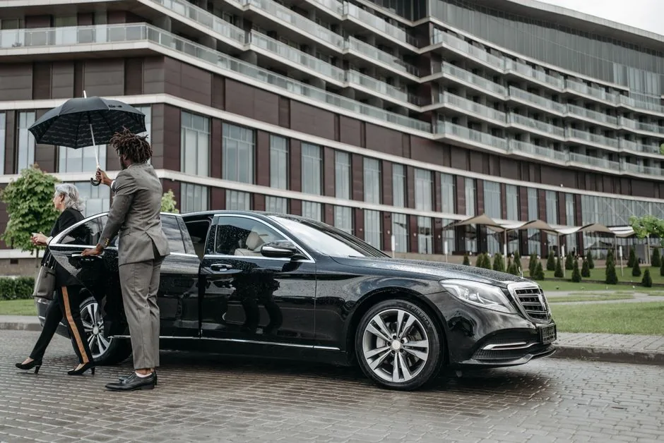 Chauffeur holding an umbrella and the door of a black sedan for a passenger