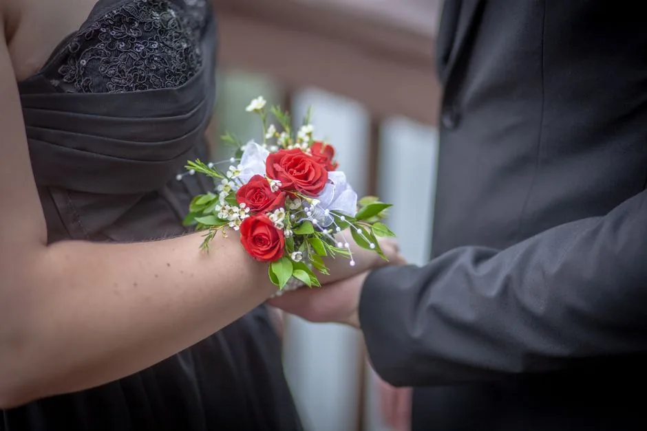 Red rose corsage on a wrist beside a dark suit