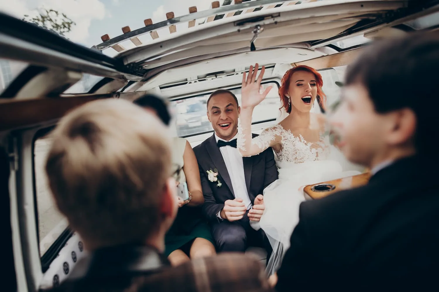 Bride and groom laughing with guests in the back of a limousine