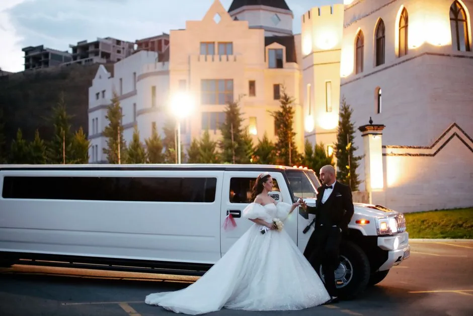 Bride and groom beside a white Hummer stretch limousine outside a lit venue at dusk