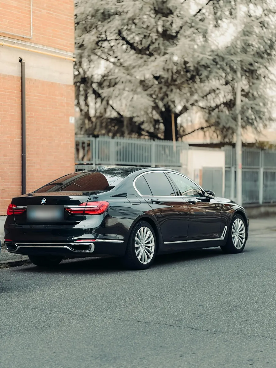 Black BMW 7 Series sedan parked on a street beside a brick building