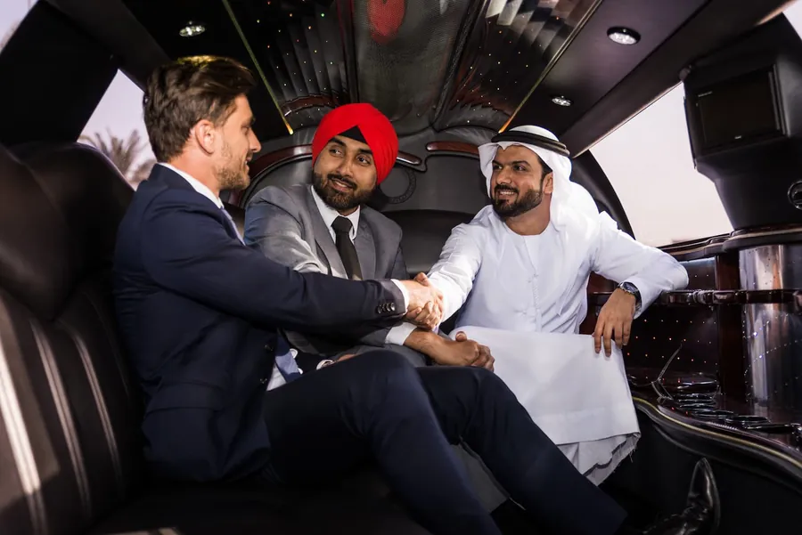 Three business travelers shaking hands in the back of a stretch limousine