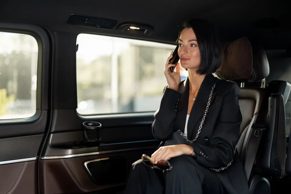 Woman in a black suit taking a phone call in the back seat of a chauffeured van